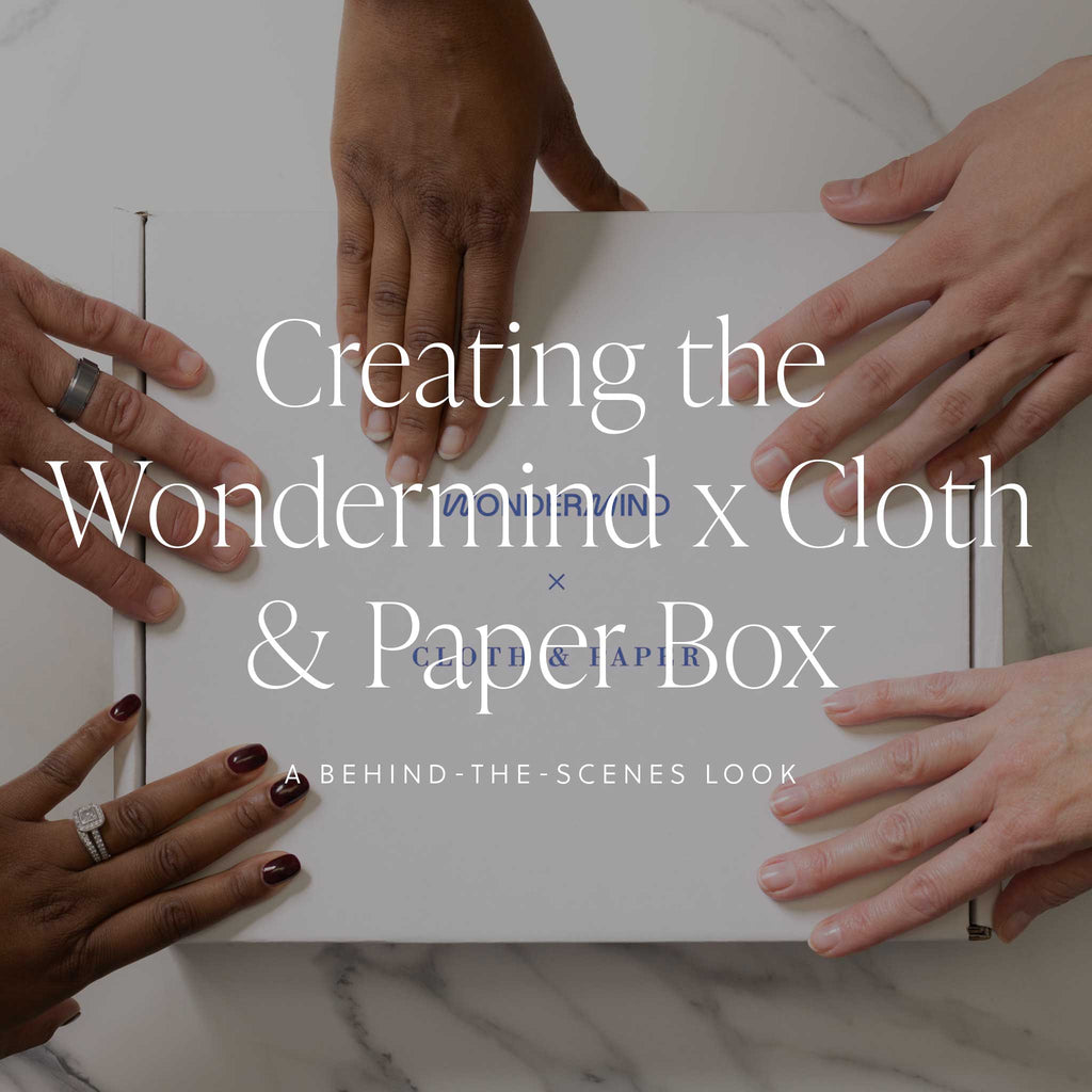 An image of a white Cloth & Paper box being touched by five hands around its sides, with a text overlay that reads: "Creating the Wondermind x Cloth & Paper Box: Behind the Scenes."