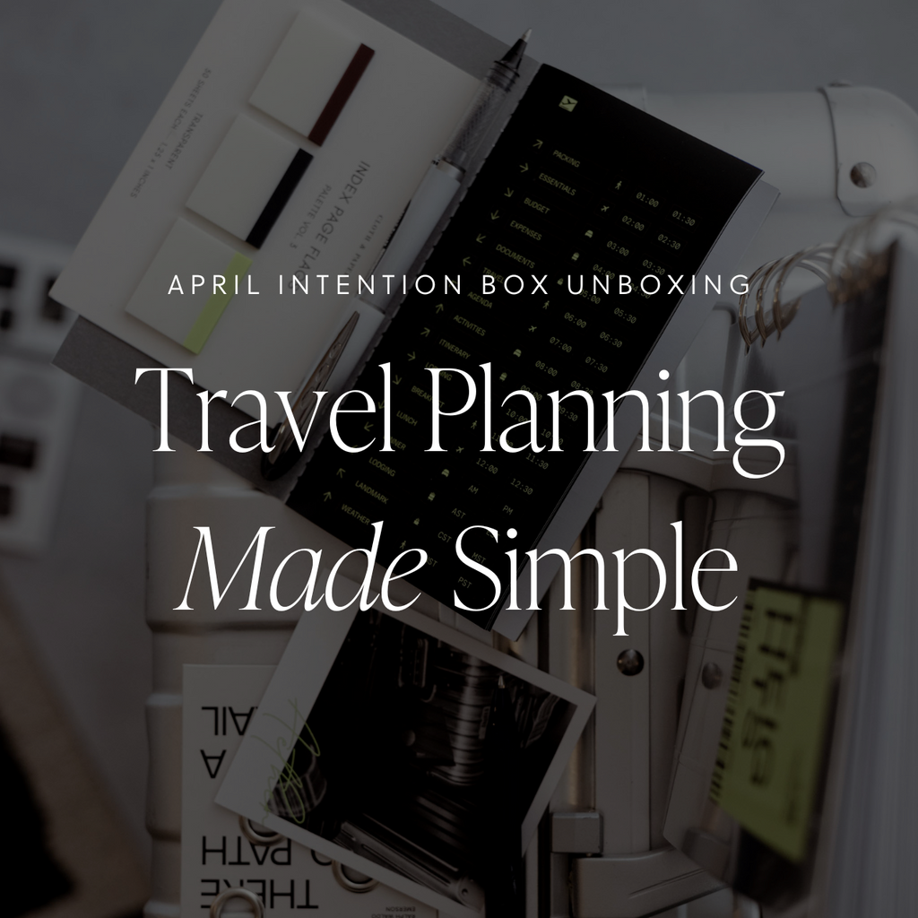 An open black sticker notebook, page flags and journaling card resting on a white suitcase, with a text overlay that reads: 'April Intention Box Unboxing: Travel Planning Made Simple.' 