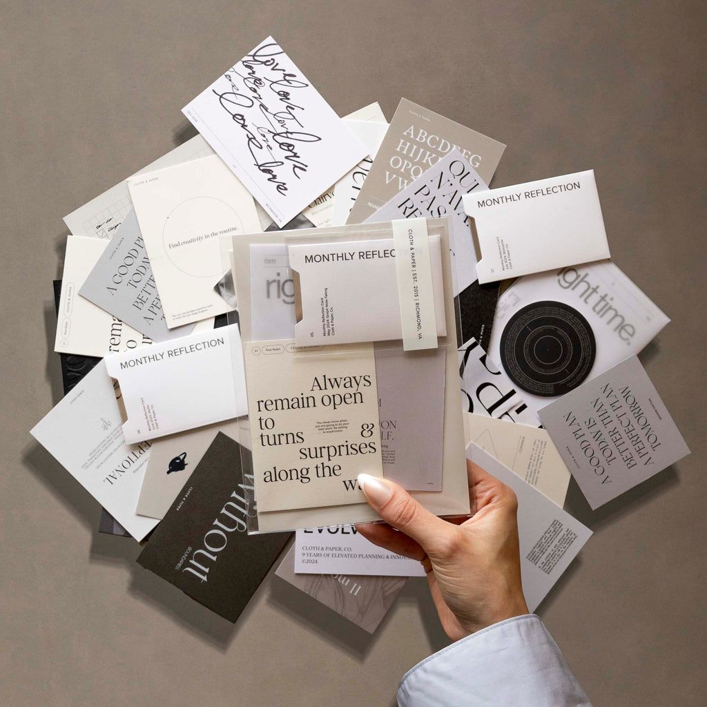 The foreground shows a hand holding a set of assorted journaling cards. The background shows a stack of assorted journaling cards.