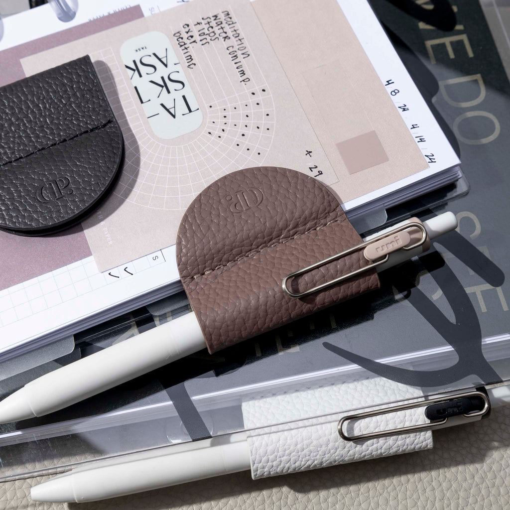 Image shows three variants of the eCLIPse Leather Bookmark Pen Holders used to clip pens onto some planners.