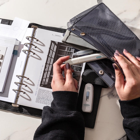 An image representing some spoilers of our October Penspiration and Planning + Stationery subscription box. A pale hand is shown pulling a highlighter from a Double Carryall Pouch. Also visible are Column Note Taking Planner Inserts, a journaling card, and Correction Tape Pen. 