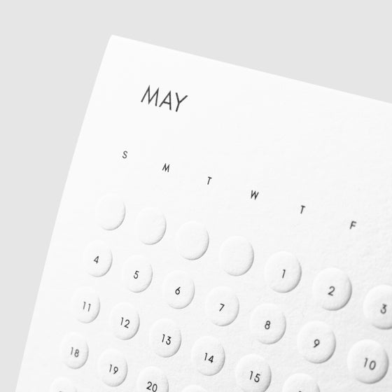 Closeup of calendar showing printed black text and embossed round circles noting each day of the week.