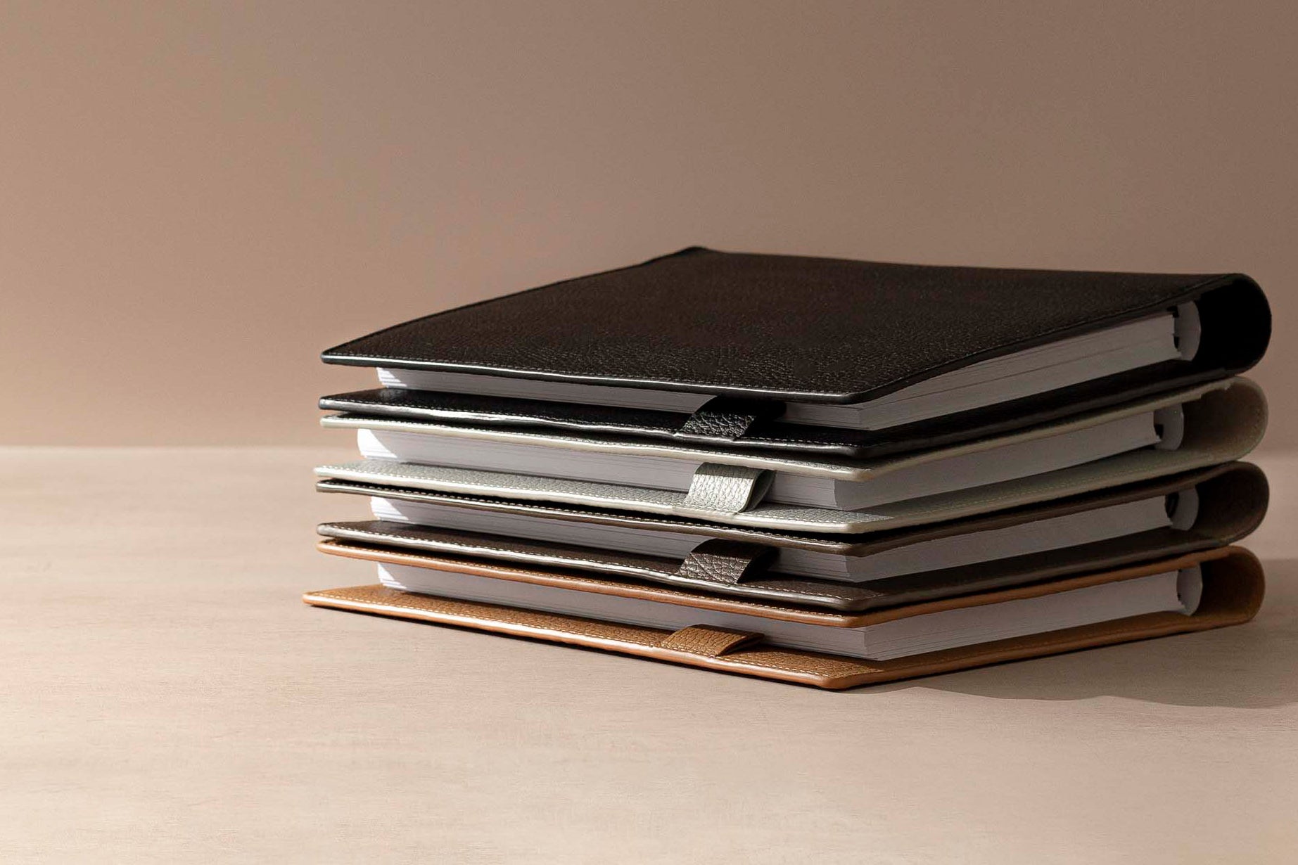 Heirloom Leather Folios in HP Classic are stacked on a desk against a light brown background.  Inside the Folios are España Spiral Notebooks in HP Classic.