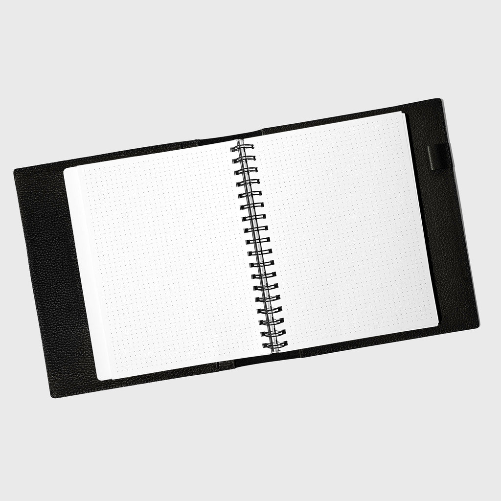 Notebook spread open inside a black leather agenda. Design shown is dot grid.