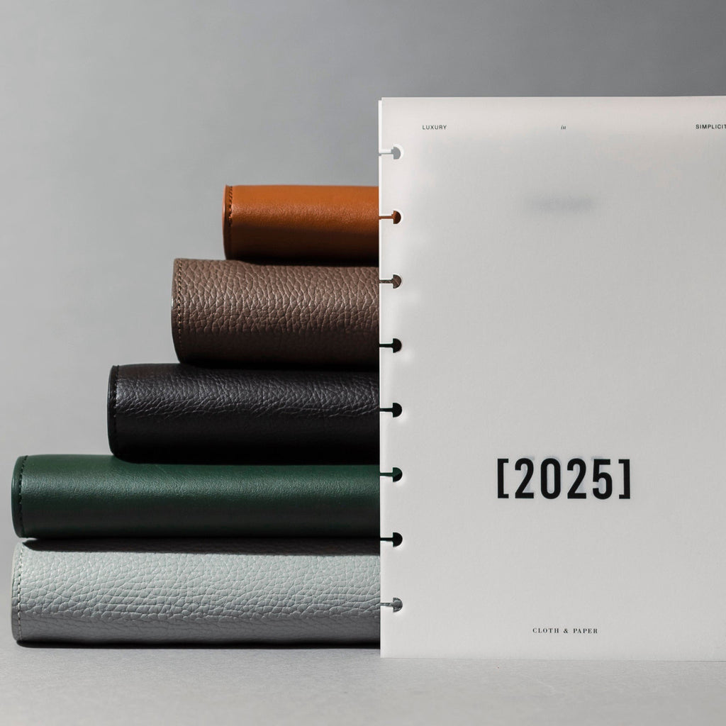 A 2025 Front and Monthly Vellum Dashboard Overlay is standing up in front of a stack of Leather Folios.
