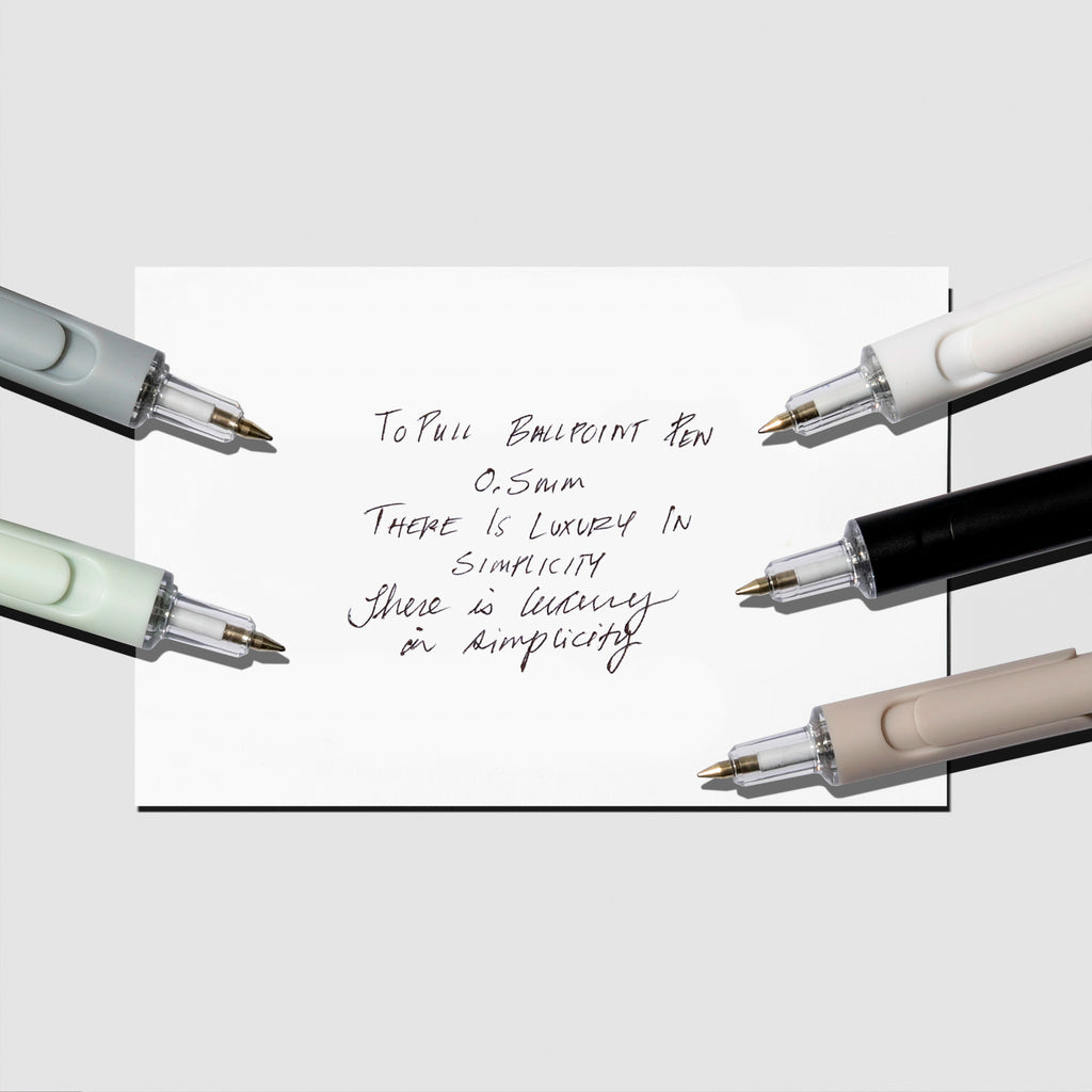 Writing sample displayed with beige, black, blue, mint, and white pens on a neutral background.