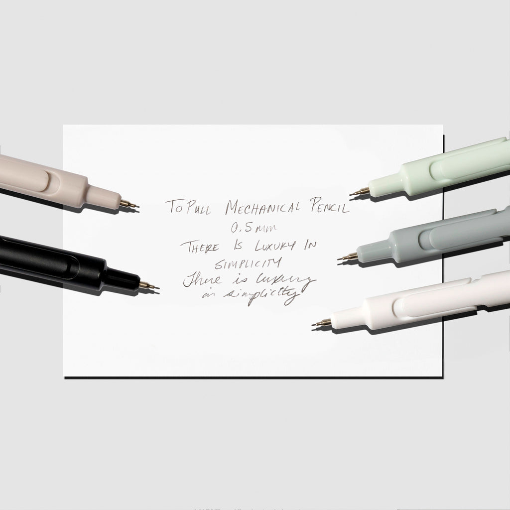 Writing sample displayed with beige, black, mint, blue, and white pencils on a neutral background.