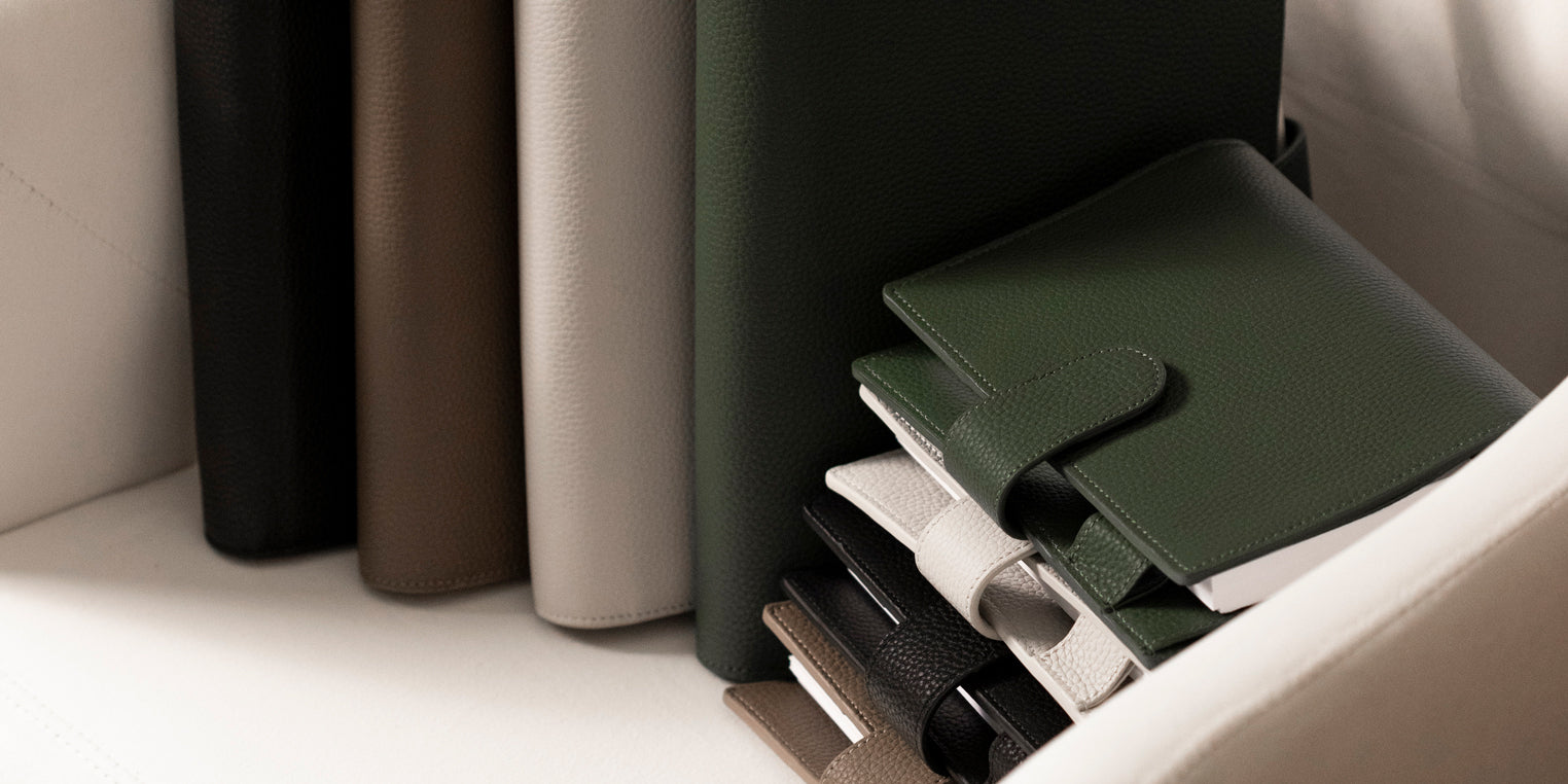 Several Foundations 6-Ring Leather Agendas in a variety of colors are sitting on a white chair.