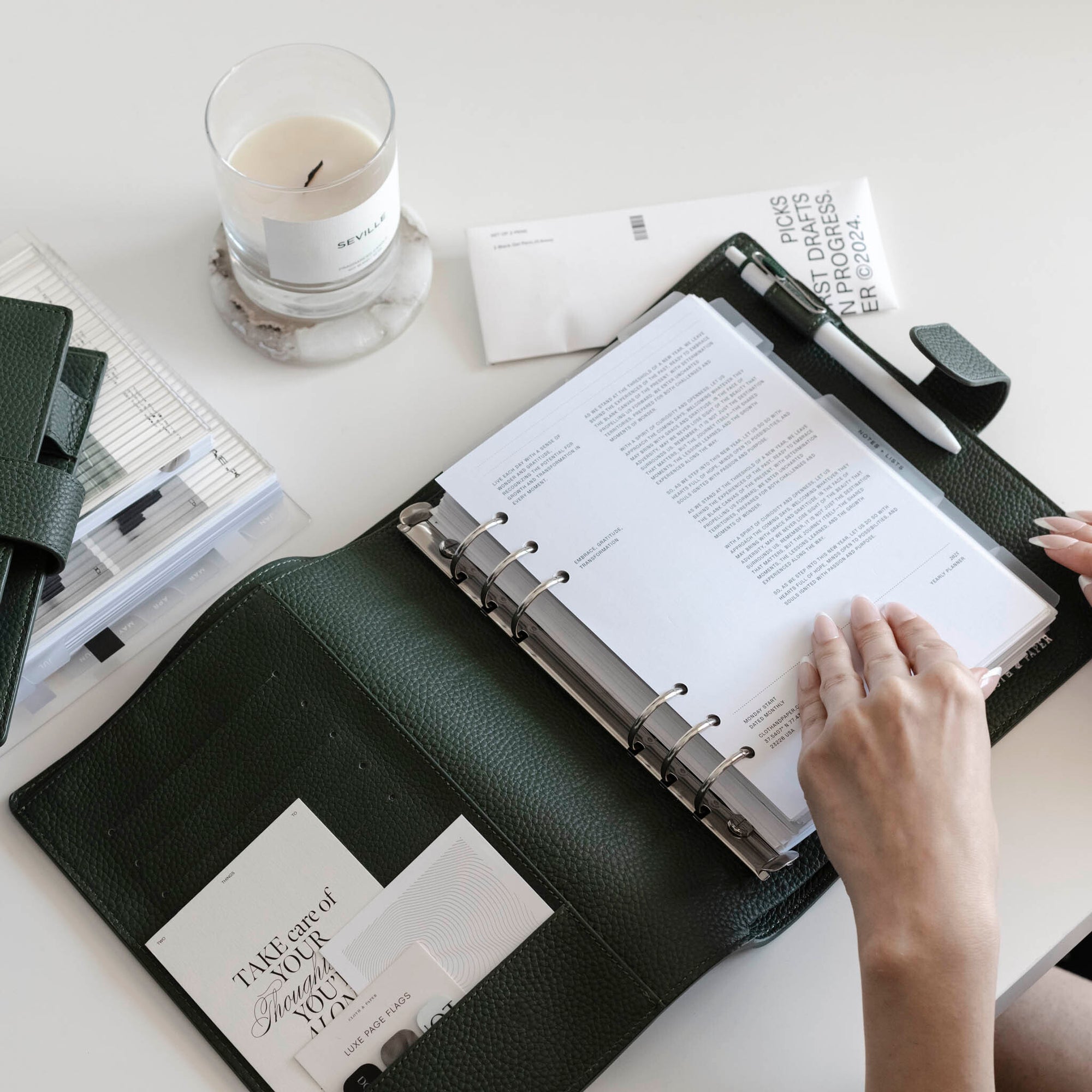 An Image of an open Foundations Leather Planner on a white desk surrounded by various planner accessories