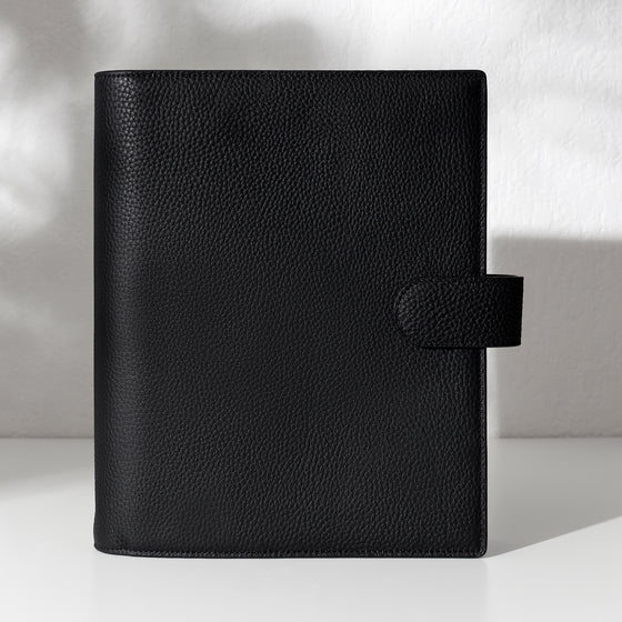 Black leather agenda displayed on an off-white background.