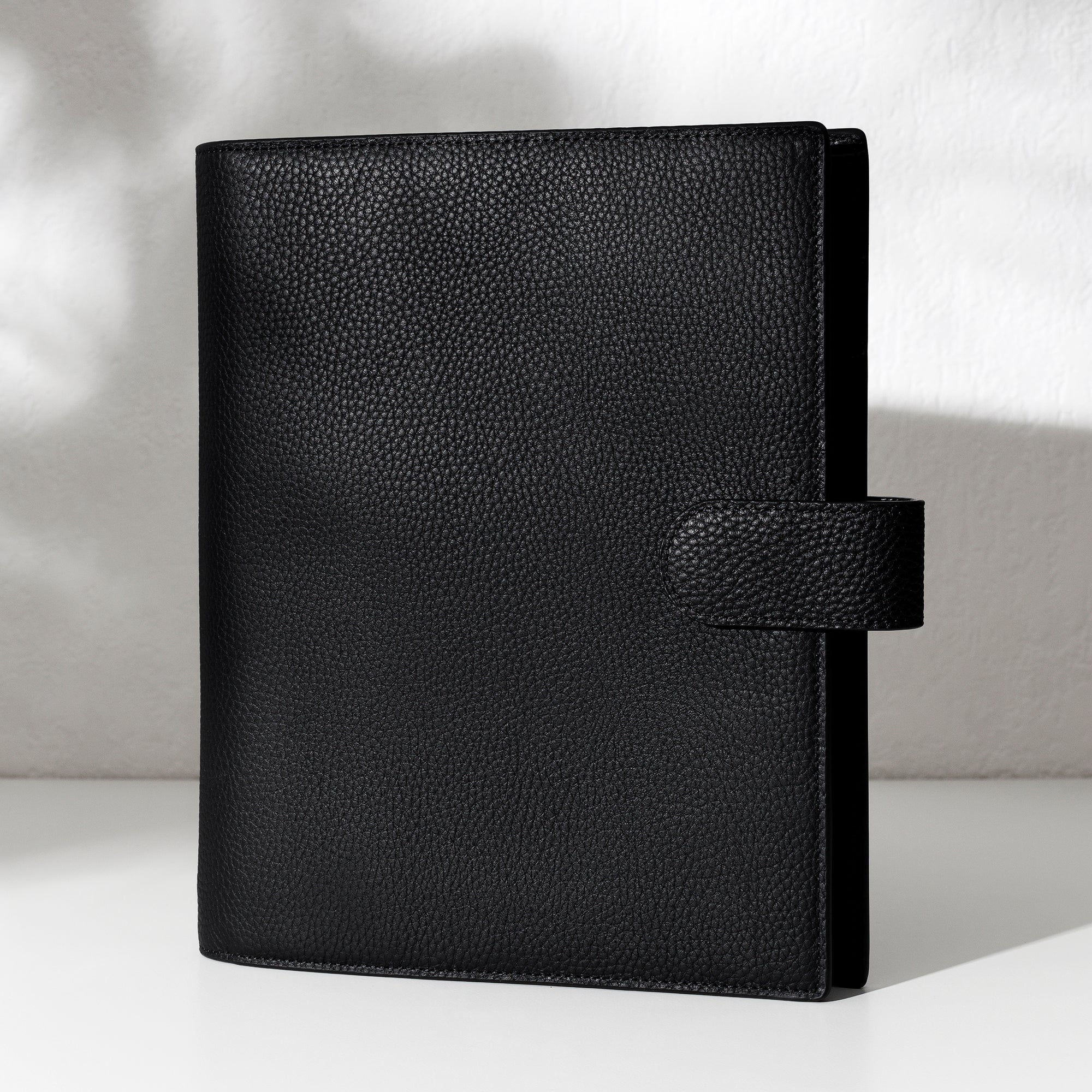 Black leather agenda displayed on an off-white background.