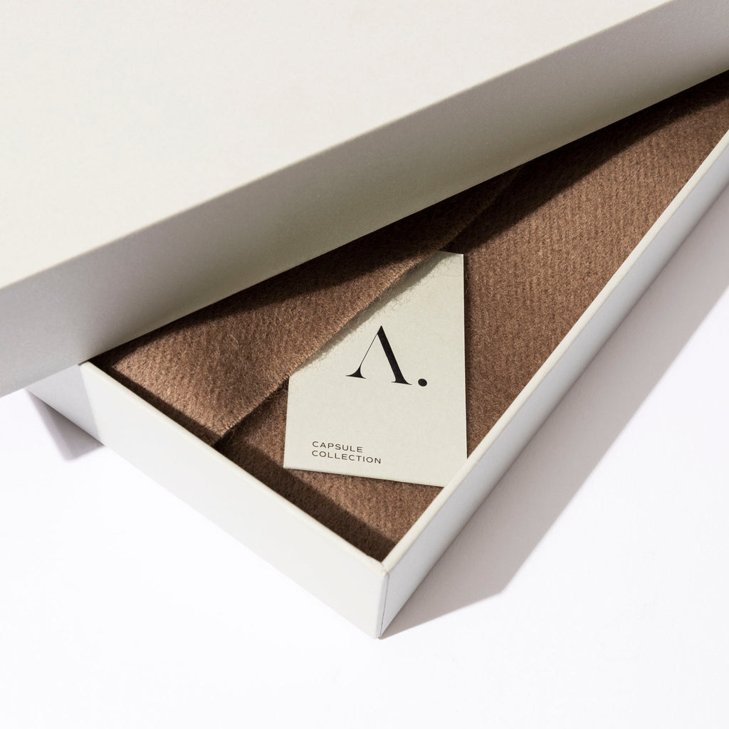 Scarf displayed in its box. An Aesthete capsule collection tag is visible.