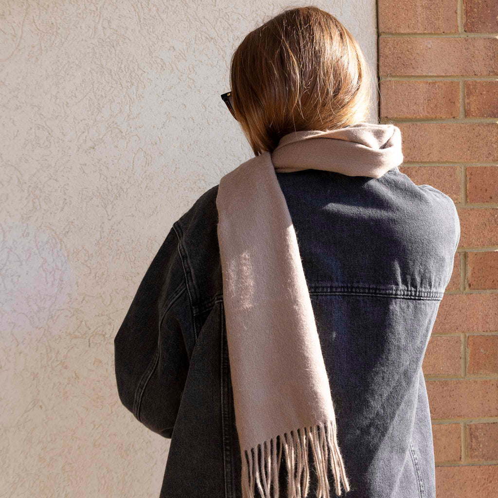 Model shown wearing the Merino wool scarf. She has brown hair, a black jacket, and is lit from the side.