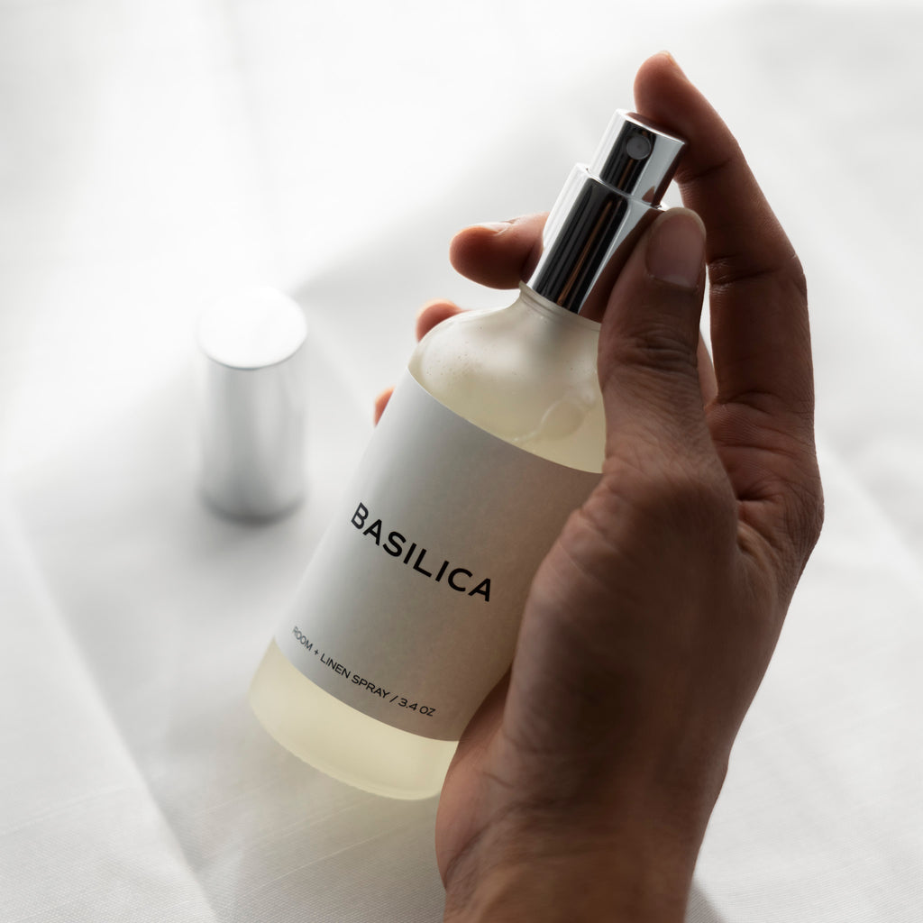 A hand is holding a bottle of the Basilica Room Spray.