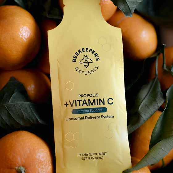 A vitamin C supplement dissolving in a glass of orange juice, branded as Beekeeper's natural supplement.