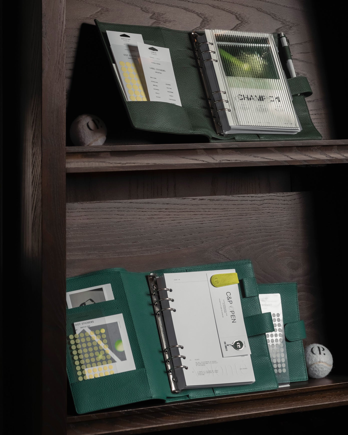 A couple 6-Ring Leather Agendas are sitting on a brown bookshelf with other CP Open Collection planner accessories present.  