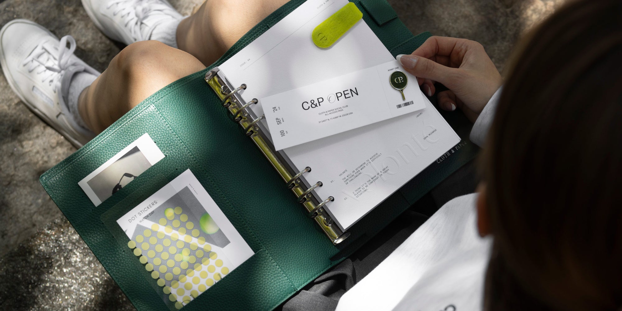 A person is sitting on a step outside with an opened 6-Ring Leather Agenda.  Inside the agenda there are several C&P Open Collection planner accessories.