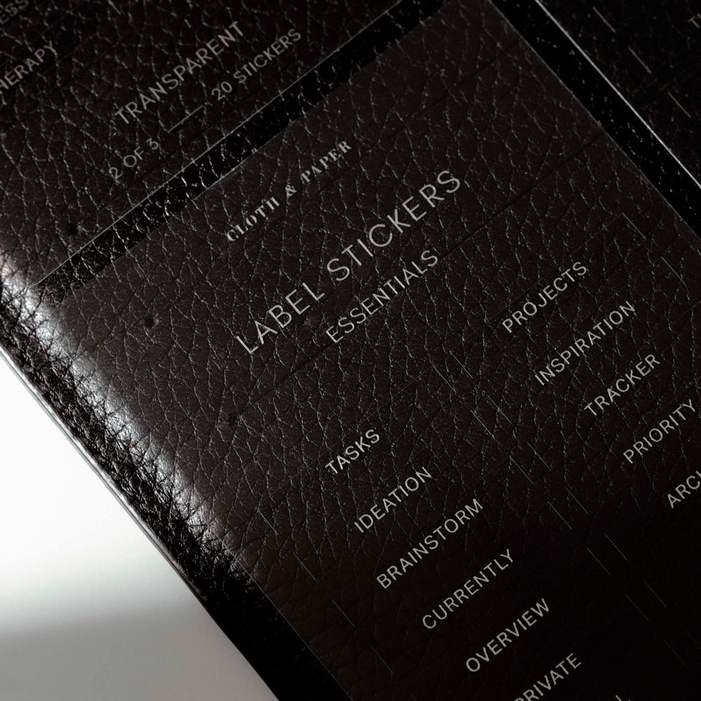 Close up image of the Clear Label Stickers against a black leather planner, which is titled to slight angle to the left