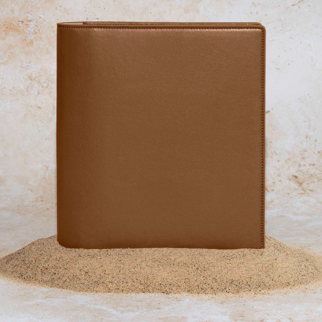 Folio displayed on a textured tan background, placed in a pile of sand. Color pictured is clay brown. 