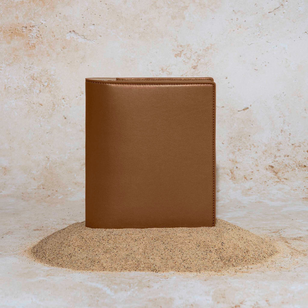 Folio displayed on a textured tan background, placed in a pile of sand. Color pictured is clay brown.