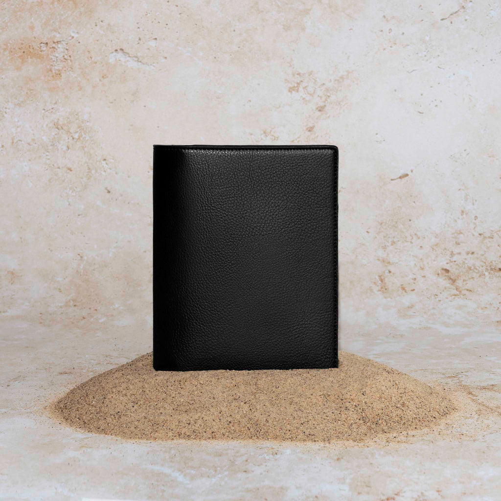 Cactus Vegan Leather Folio, CP Petite, Cloth and Paper. Folio displayed on a textured tan background, placed in a pile of sand. Color pictured is mesa black.