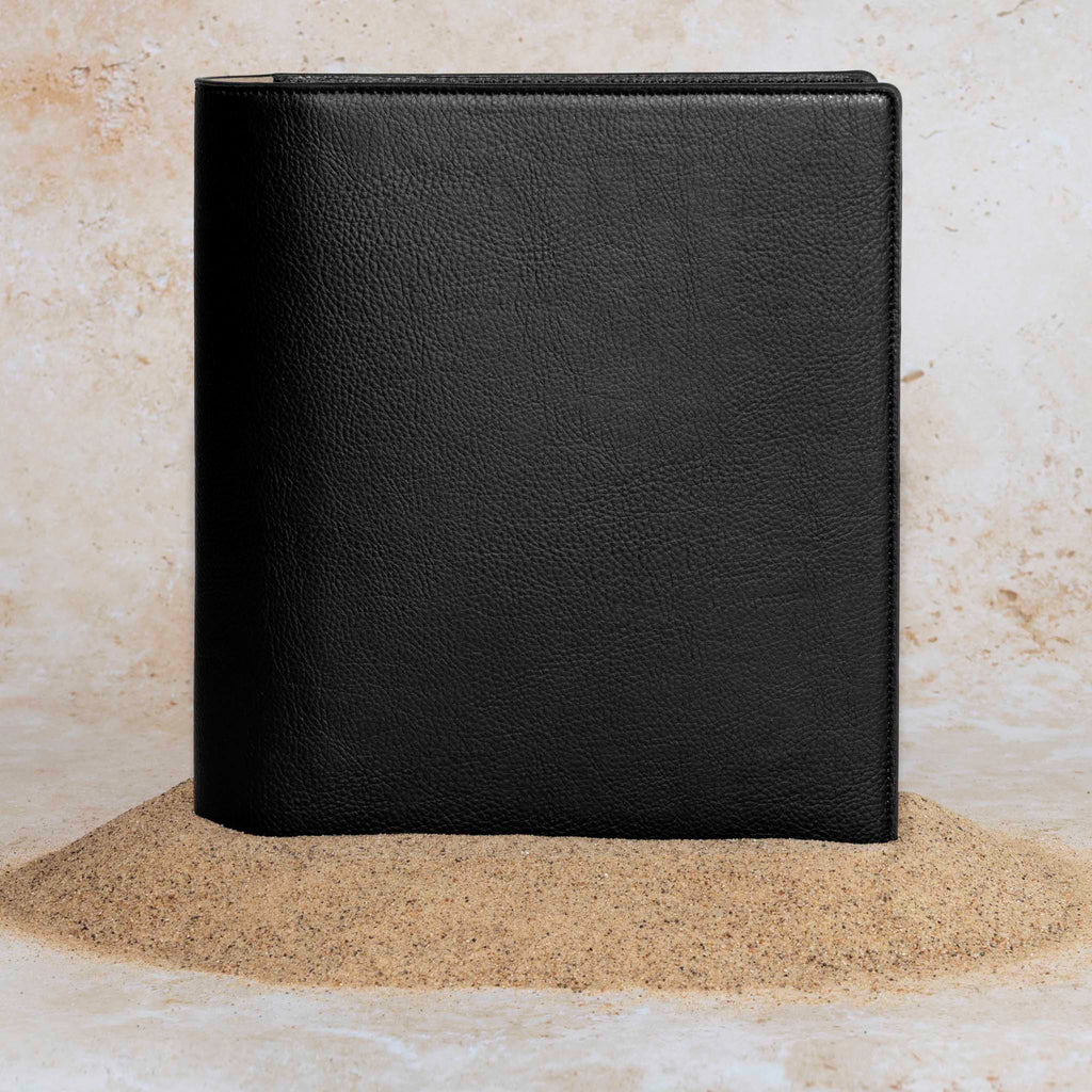 Cactus Vegan Leather Folio, HP Classic, Cloth and Paper. Folio displayed on a textured tan background, placed in a pile of sand. Color pictured is mesa black.