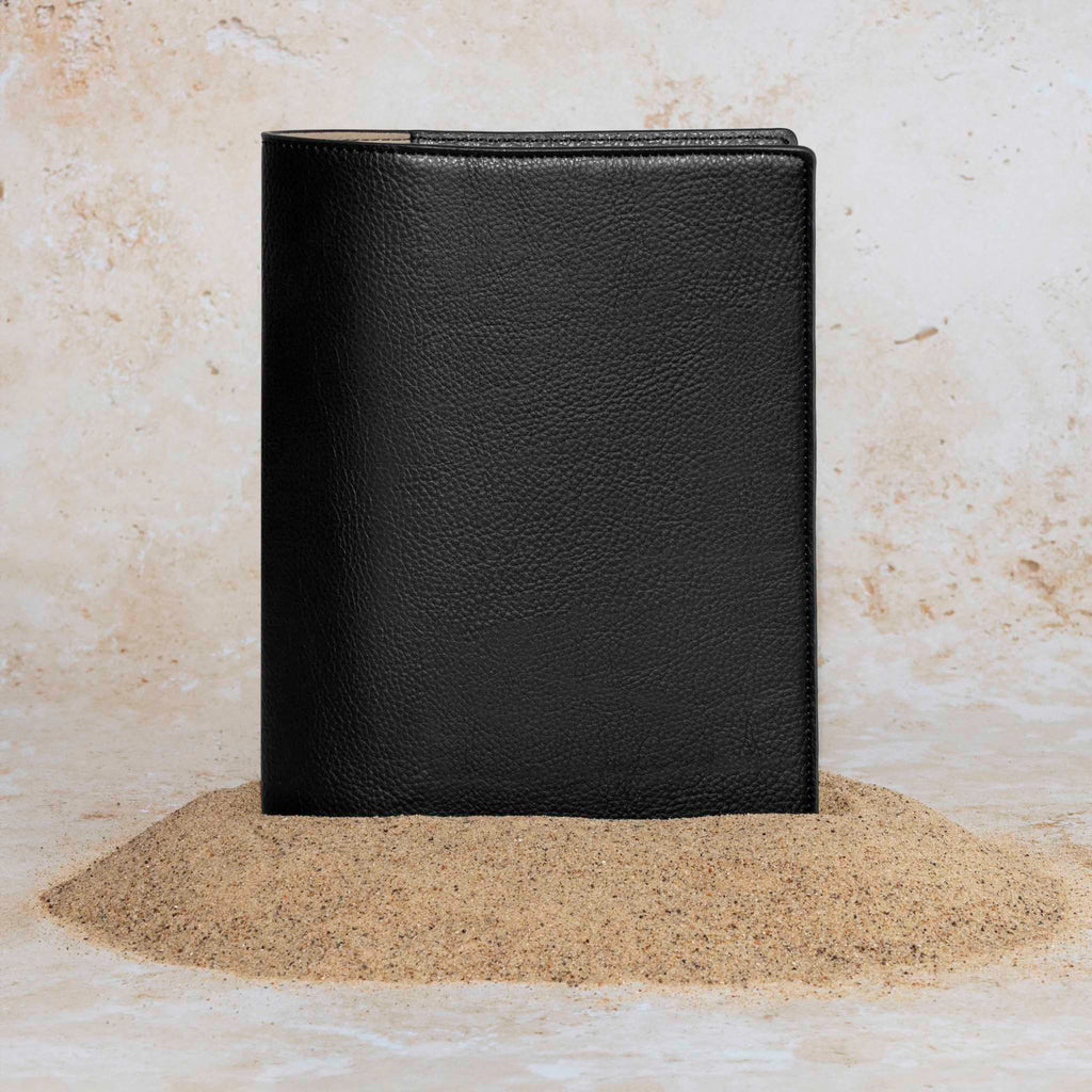 Cactus Vegan Leather Folio, Half Letter, Cloth and Paper. Folio displayed on a textured tan background, placed in a pile of sand. Color pictured is mesa black.