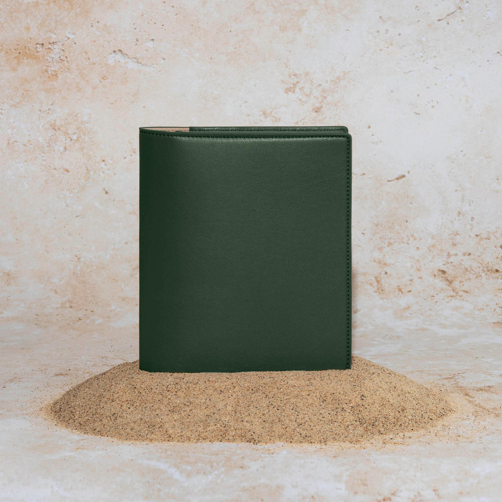 Folio displayed on a textured tan background, placed in a pile of sand. Color pictured is valley green.