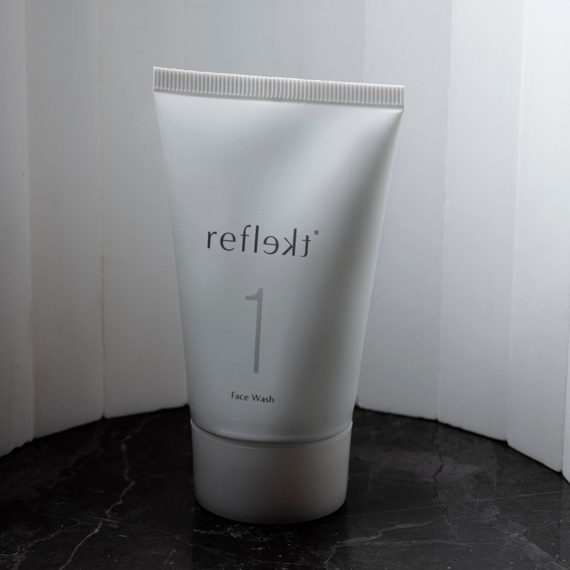 A container of Daily Exfoliating Face Wash by Reflect is standing up against a white background.  There is a slight shadow over the product.