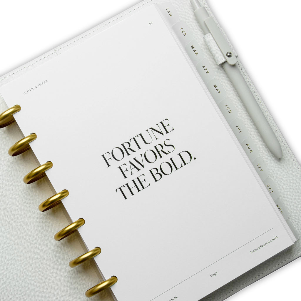 Fortune Planner Dashboard styled inside a white leather agenda cover. The cover has a beige pen in its pen loop.