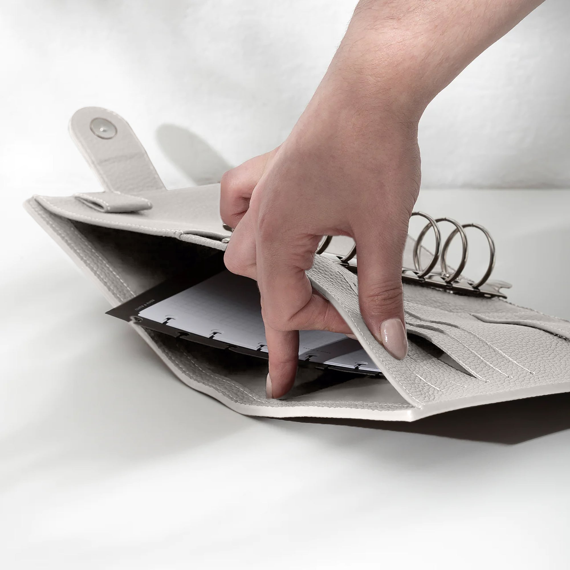 A fair-skinned hand shown opening the back pocket of the agenda on a white background. There are inserts and a dashboard inside the pocket.