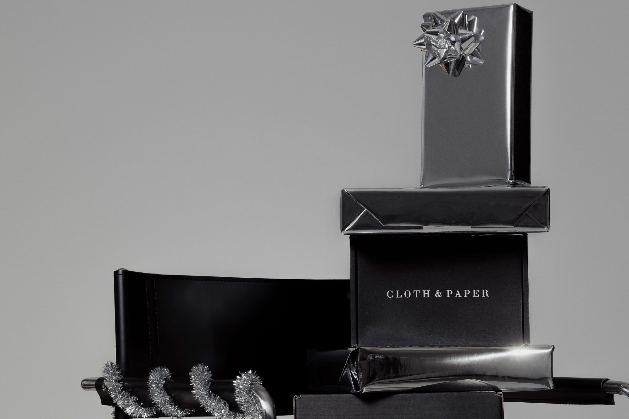 Black and silver gift boxes stacked on top of each other sitting in a black chair, with a "CLOTH & PAPER" label on one of the boxes.