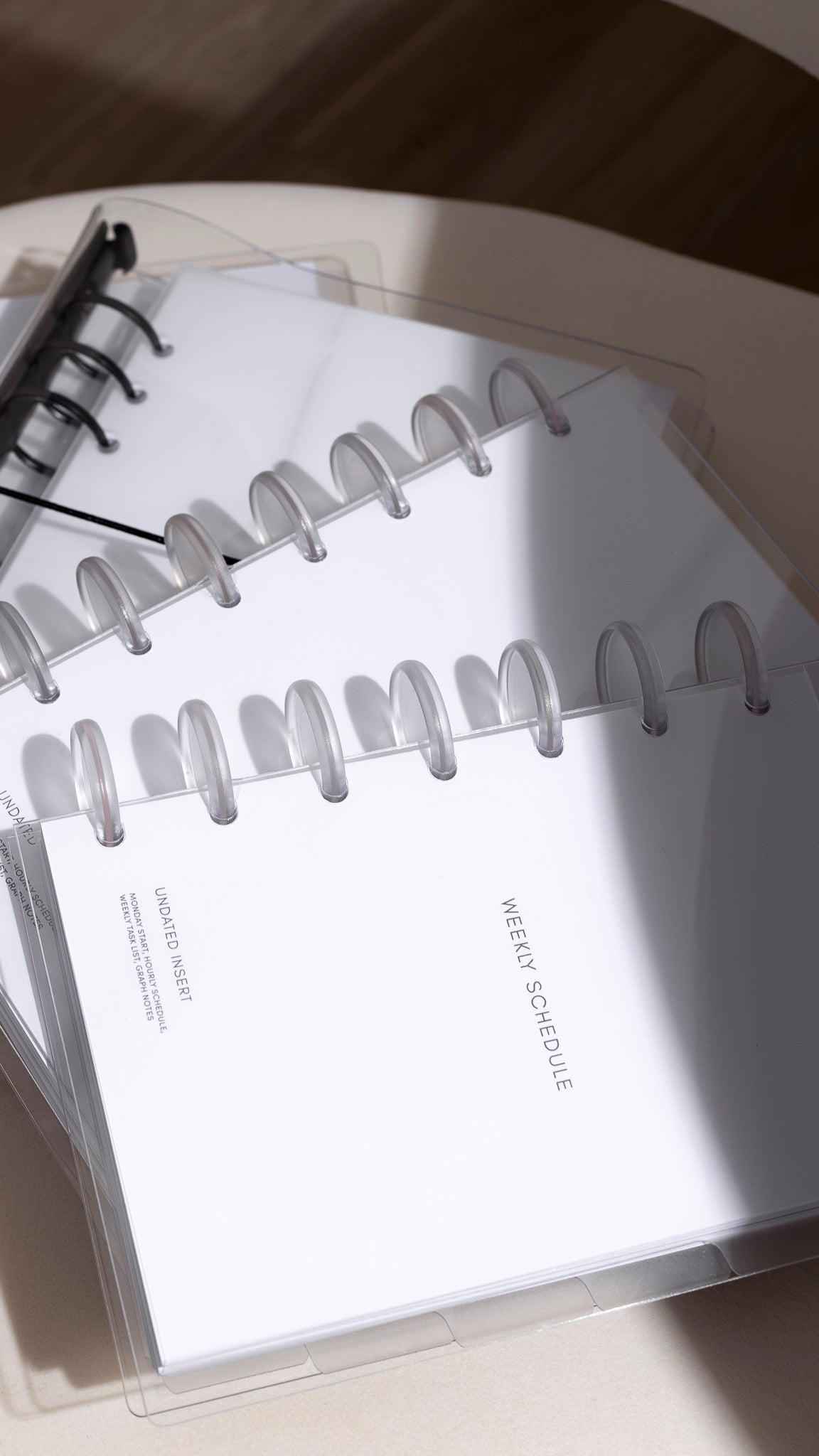 A stack of white ringbound and discbound planners with transparent covers, showing a "WEEKLY SCHEDULE" page.