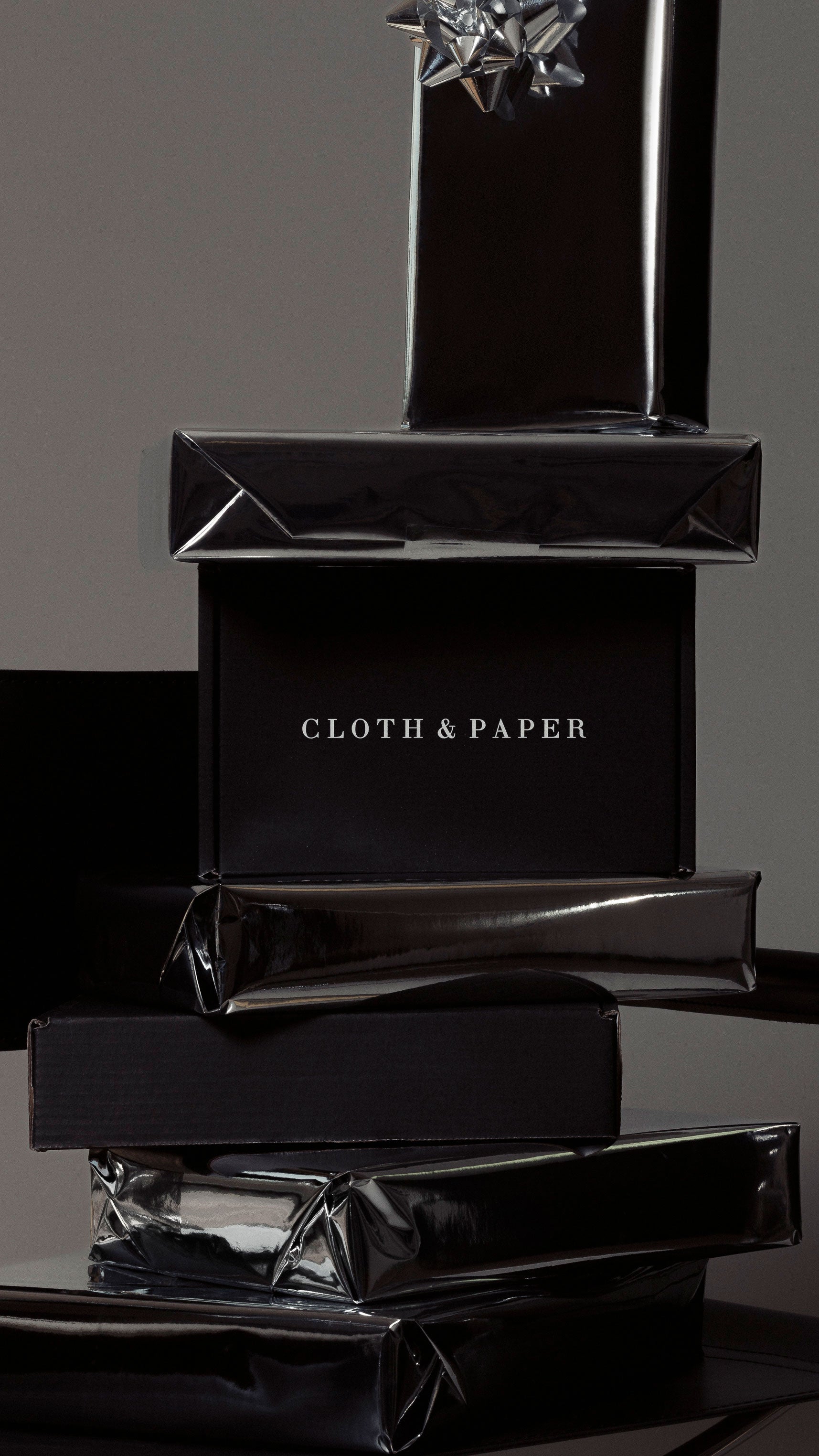 Black gift boxes stacked on top of each other, with a "CLOTH & PAPER" label on one of the boxes.