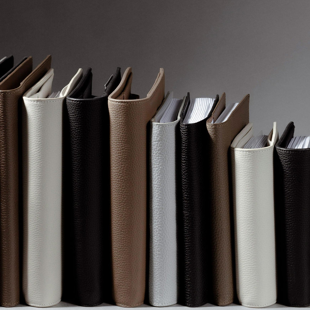 An image representing some of our Heirloom Premium Leather Folios.  The different folios and colors are standing up side by side with their spines facing out against a gray background.