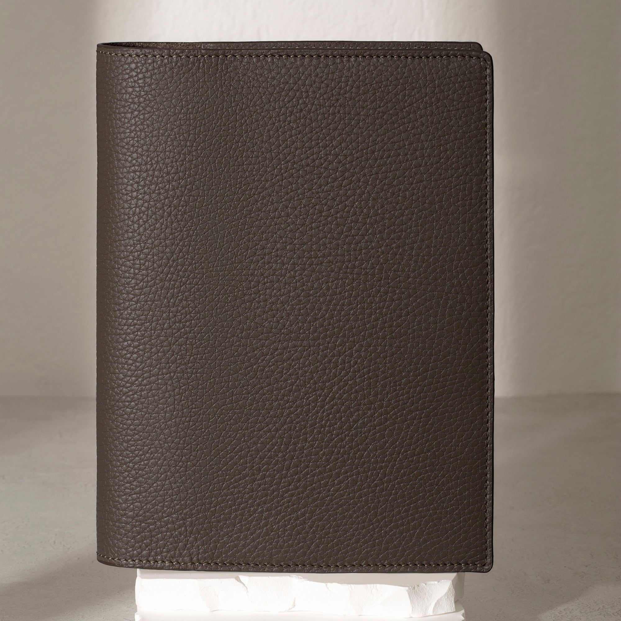 Large Leon folio displayed on a white stone pedestal. The background is a natural textured off-white material, and a spotlight behind the folio highlights its placement.