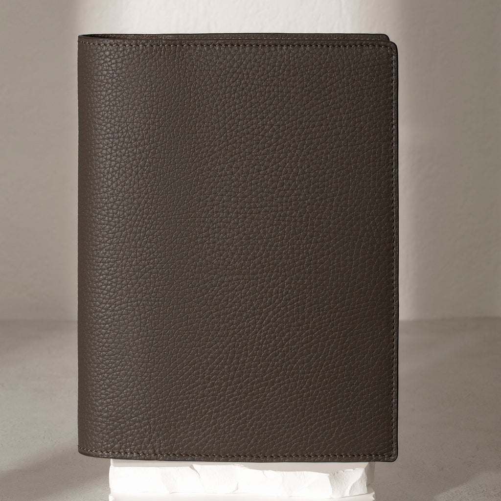 Large Leon folio displayed on a white stone pedestal. The background is a natural textured off-white material, and a spotlight behind the folio highlights its placement.