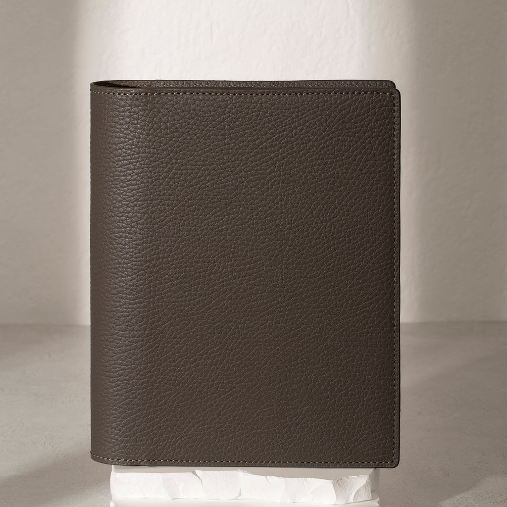 Small Leon folio displayed on a white stone pedestal. The background is a natural textured off-white material, and a spotlight behind the folio highlights its placement.
