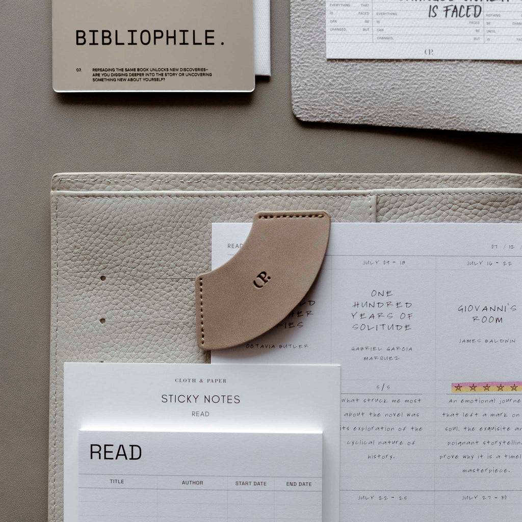 Bookmark in use inside of a leather planner. The planner is surrounded by sticky notes, an insert, and journaling cards.