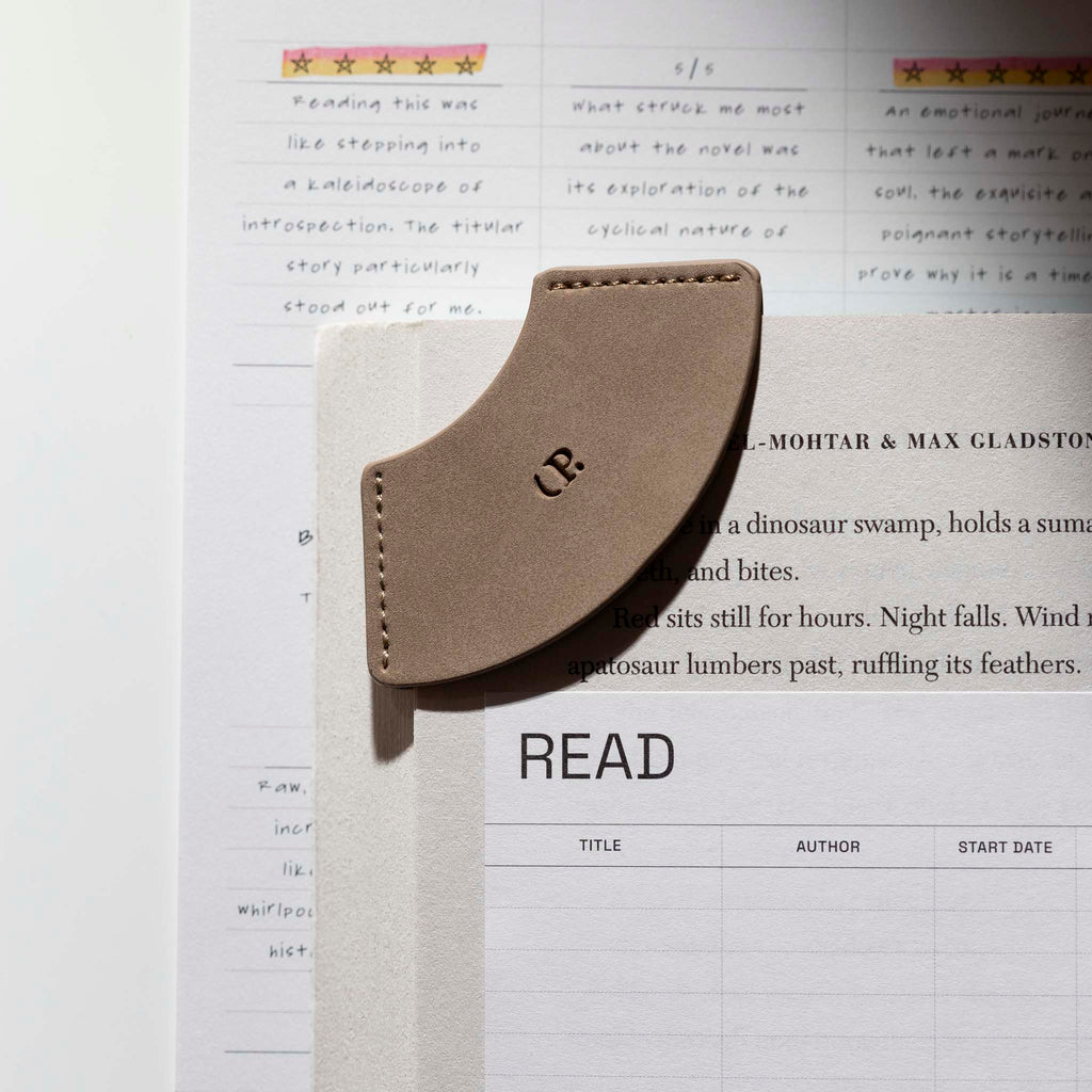 The new Vegan Leather Bookmark is attached to a page in a book with other surrounding planner accessories.
