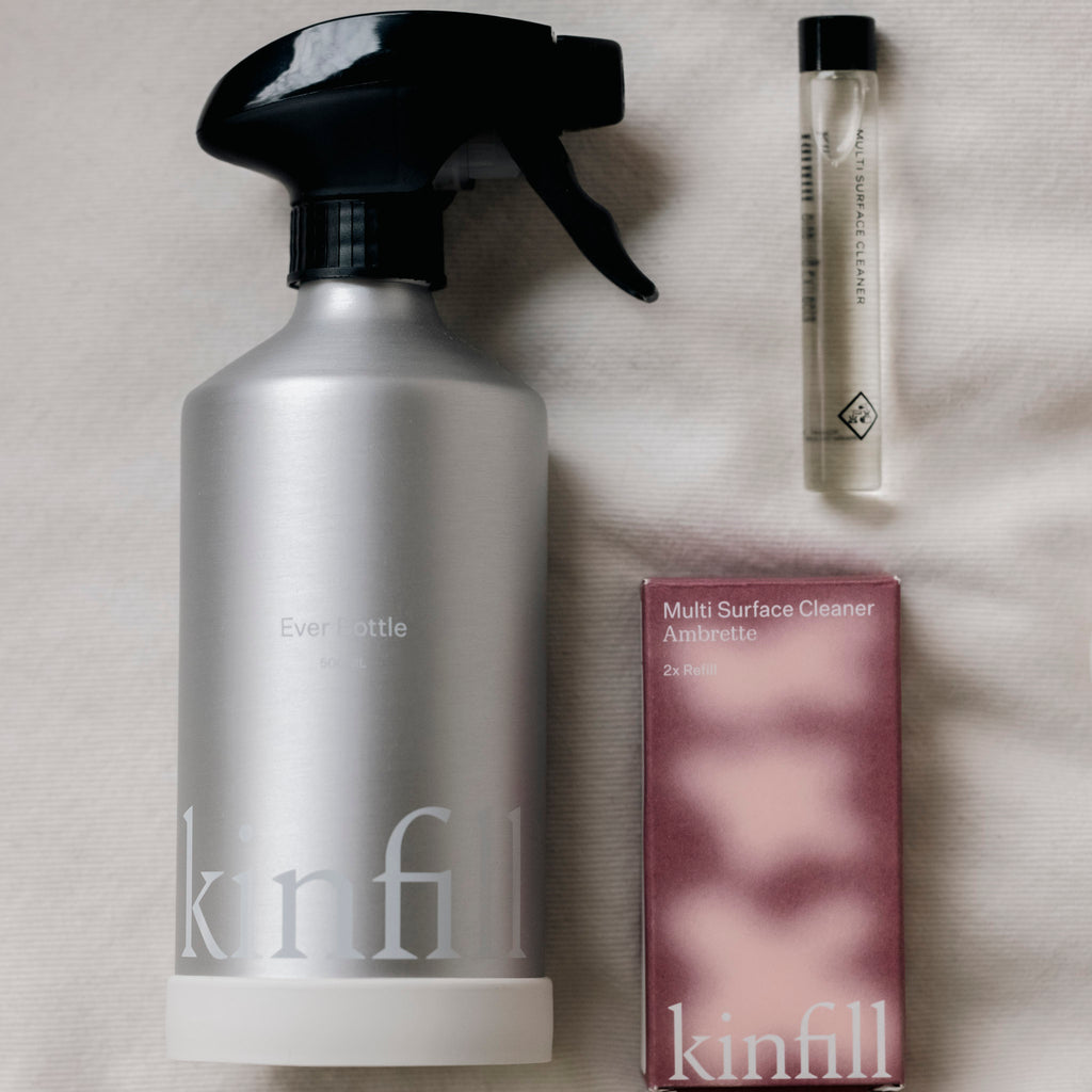 Kinfill Cleaner kit displayed on a bed, featuring a spray bottle and a box of soap among the products.