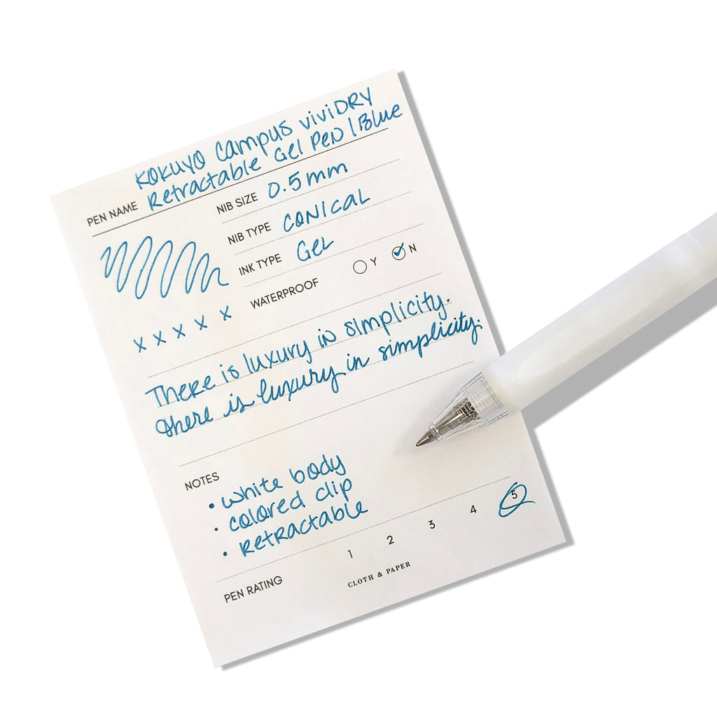Kokuyo Campus viviDRY Retractable Gel Pen | Blue | Cloth & Paper. Pen resting on pen test sheet displaying writing sample.