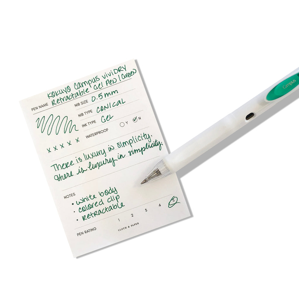 Kokuyo Campus viviDRY Retractable Gel Pen | Green | Cloth & Paper. Pen resting on pen test sheet displaying writing sample.