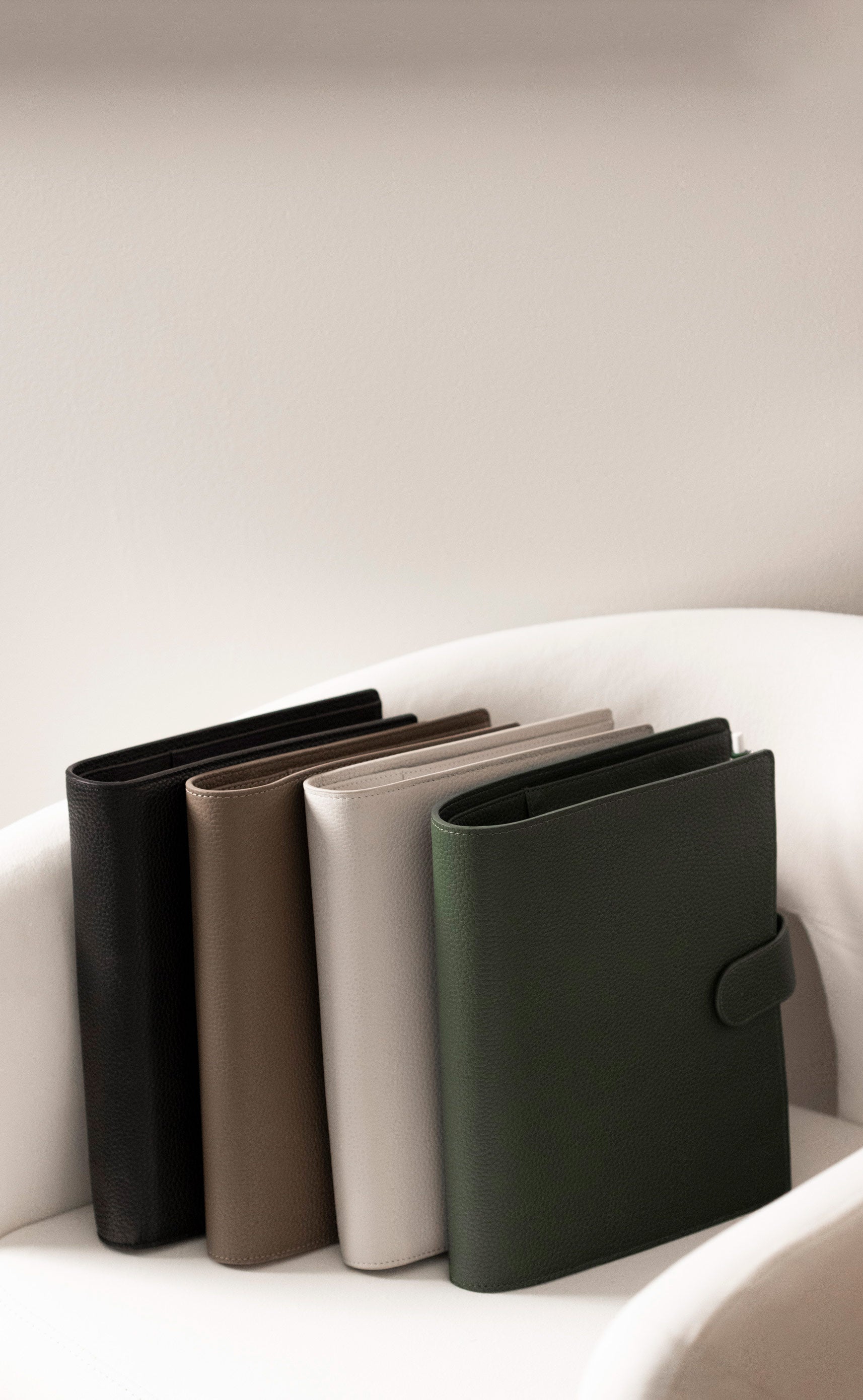 Several Foundations 6-Ring Leather Agendas in a variety of colors are sitting on a white chair.