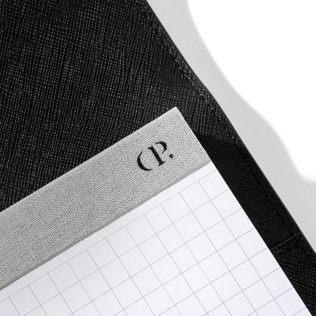 Closeup of Cloth and Paper "CP" logo printed on the fabric spine of the notepad.