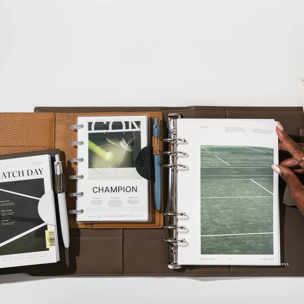 An image representing our new Luxe Sports Dashboards. Each issue is layered inside an opened leather planner with other surrounding planner accessories.