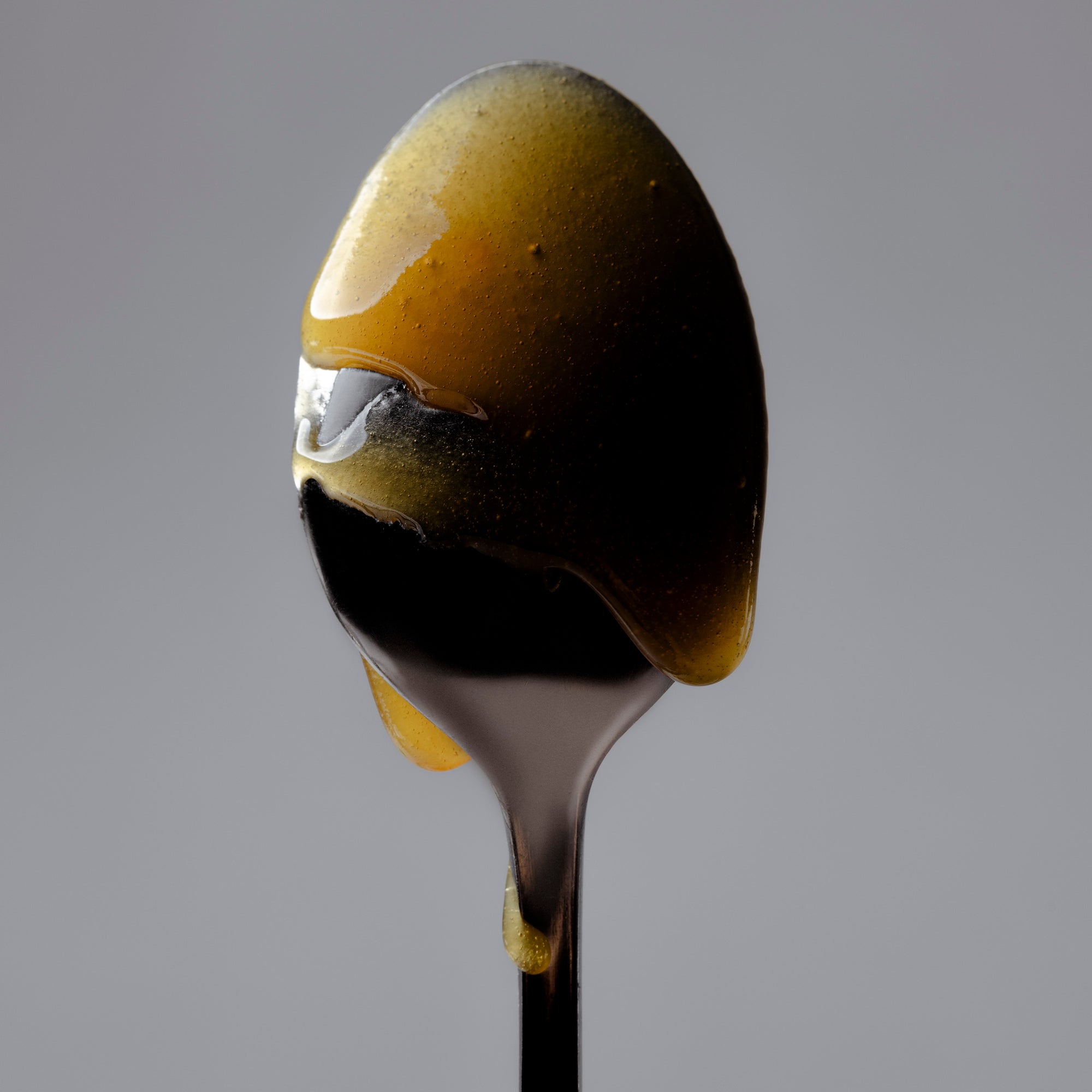 The back of a spoon dripping with Mānuka Health Honey. 