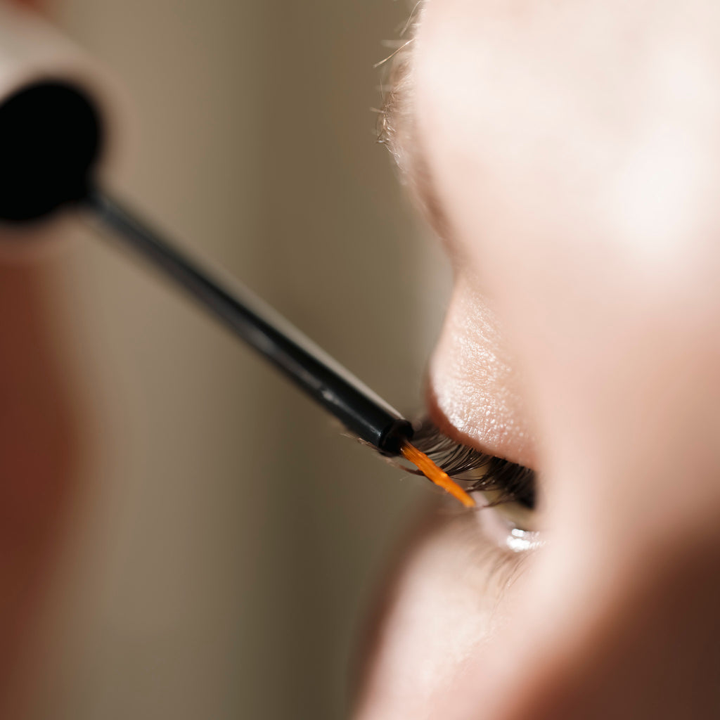 A woman carefully applies mascara to enhance her eyelashes, focusing intently on her eye in a well-lit setting.