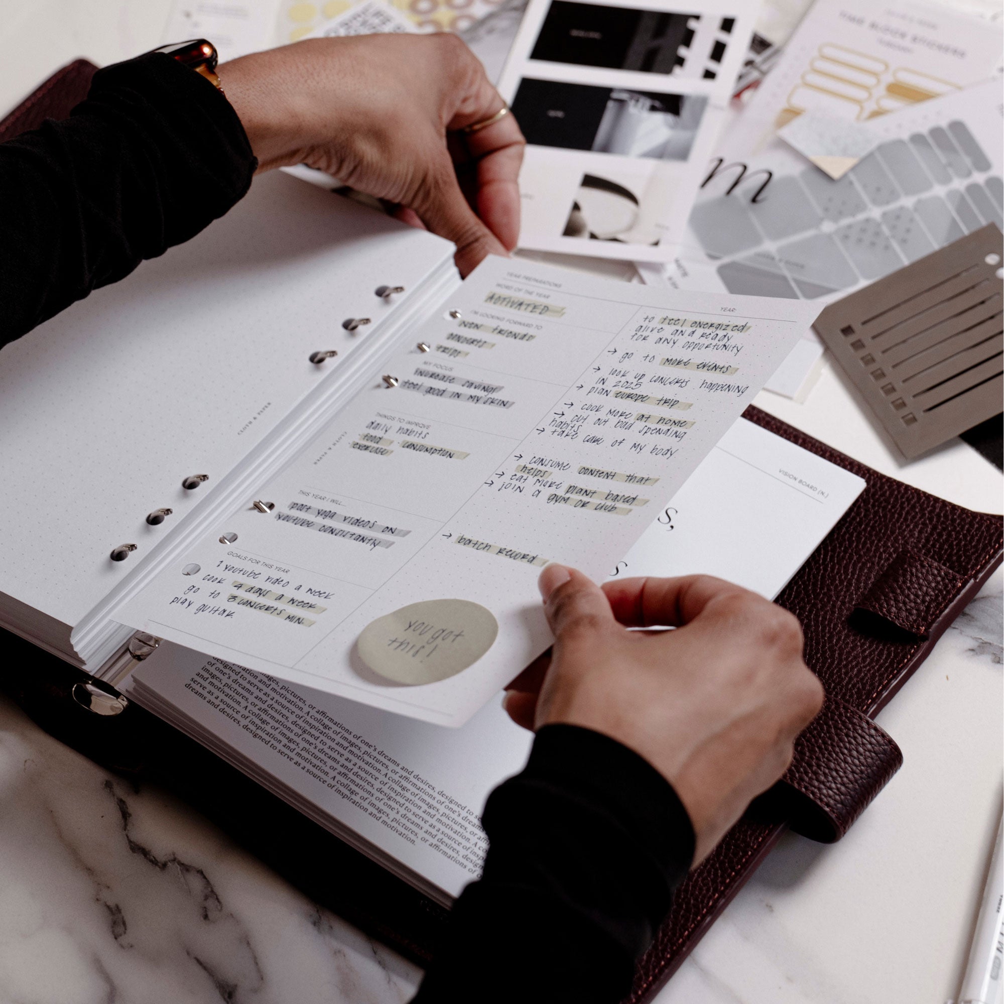 A hand is placing a planner insert inside a Foundations Leather Agenda as the planner is being set up with other surrounding accessories.