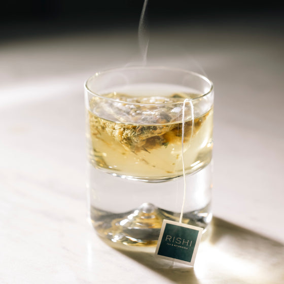 A glass of Rishi Tea with a tea bag steeping, showcasing a warm, inviting beverage ready to be enjoyed.